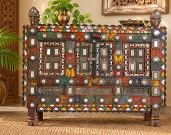 May include: A rectangular wooden cabinet featuring a multi-colored finish with red, green, yellow, and blue accents. The front surface is decorated with numerous small circular and rectangular mirrors, carved geometric patterns, and a central metal latch.