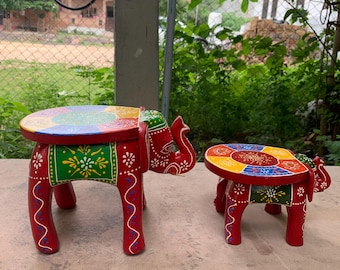May include: Two colorful wooden elephant stools, one larger than the other, with red legs and a multi-colored top. The stools are painted with intricate designs and are a vibrant addition to any home decor.