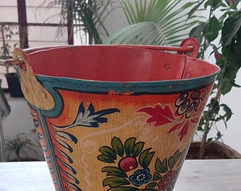 May include: A hand-painted metal bucket with a floral design in shades of yellow, red, blue, green, and pink. The bucket has a metal handle and is decorated with a traditional Indian folk art style.