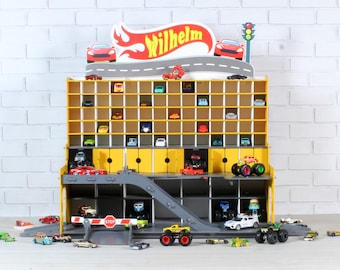 May include: A yellow and gray toy car garage with a ramp and a stop sign. The garage has multiple levels and is filled with toy cars. The garage has a sign that says "Wilhelm" on it.