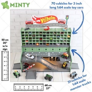 Op de afbeelding: Een groene houten speelgoedautogarage met een helling en een bord met de tekst "Wilhelm". De garage heeft 70 vakken voor 7,6 cm lange speelgoedauto's op schaal 1:64 en 21 vakken voor monstertrucks op schaal 1:64. De garage is 50 cm hoog en 68 cm breed.
