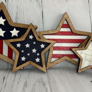 May include: A collection of wooden star-shaped decorations in various sizes. The stars feature patriotic designs, including the American flag, with red, white, and blue colors. Some stars have a wood grain border.