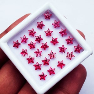 Puede incluir: Una bandeja blanca llena de veintidós piedras preciosas rojas en forma de estrella.