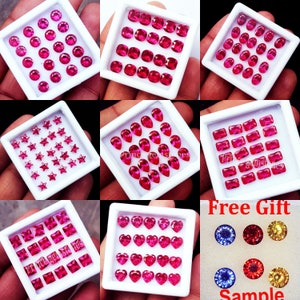 May include: A collection of vibrant red gemstones in various shapes, including round, square, oval, pear, star, and heart, displayed in white trays. A small sample of blue, red, and yellow gemstones is also included.