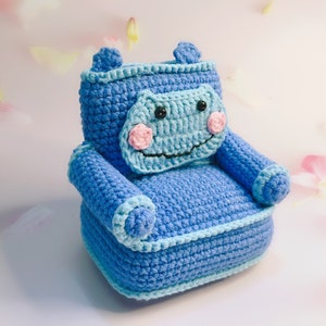 May include: A blue crocheted armchair shaped like a hippopotamus with a light blue face and pink cheeks.