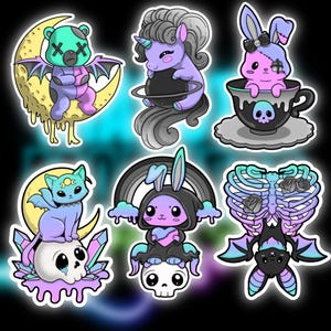 May include: A collection of whimsical, gothic-themed stickers featuring cartoon characters. Includes a bear with bat wings, a unicorn, a bunny in a teacup, a cat on a skull, a bunny under a rainbow, and a bat with a skeleton.