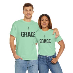 May include: Two people wearing matching light green t-shirts with the word "GRACE" in black block letters and a cross above the word. The shirts are paired with blue jeans.