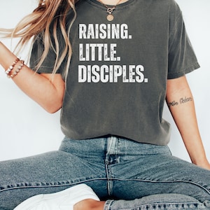 Könnte beinhalten: Ein graues T-Shirt mit dem Text "Raising. Little. Disciples." in weiß gedruckt.