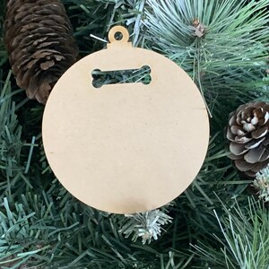 May include: A round, unfinished wooden ornament with a bone-shaped cutout. The ornament is designed for hanging on a Christmas tree.