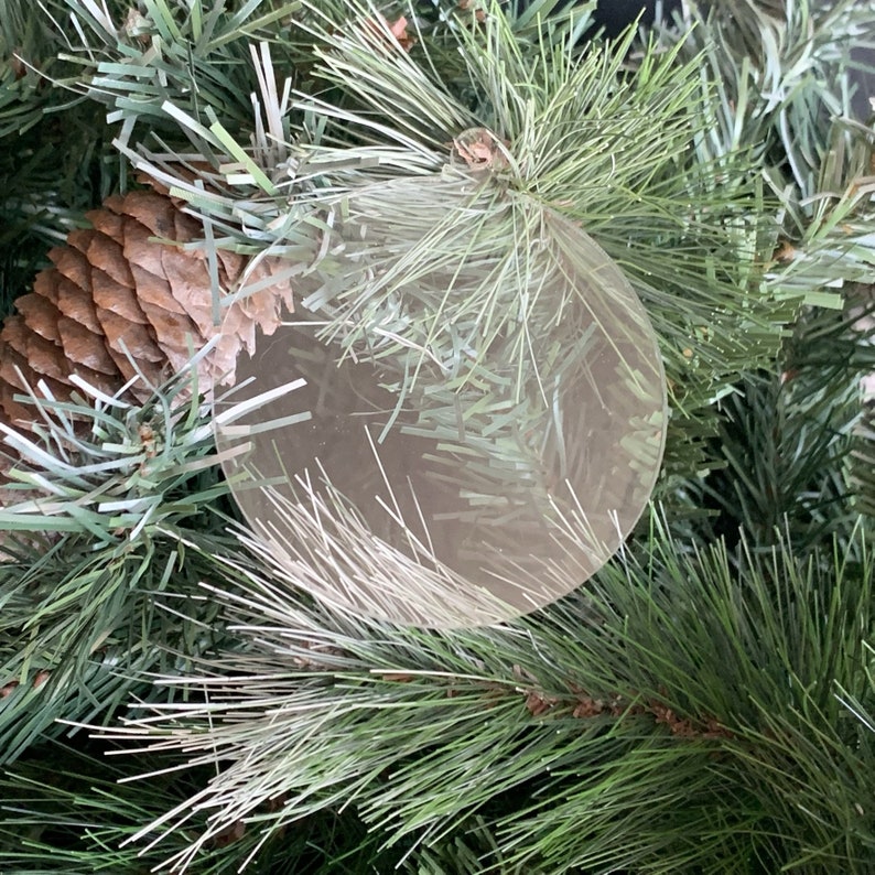May include: A close-up of a clear, round ornament hanging on a green artificial Christmas tree. The ornament is reflecting the light from the surrounding branches.