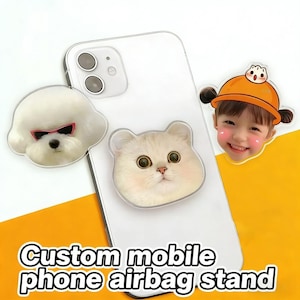 Può includere: Uno smartphone bianco con tre supporti airbag personalizzati per telefoni cellulari attaccati. I supporti presentano un cane bianco con occhiali da sole, un gatto color crema e un bambino sorridente con un cappello arancione. Il testo "Custom mobile phone airbag stand" è in basso.