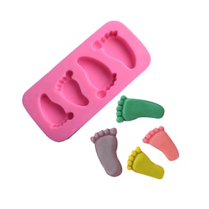 Può includere: Stampo in silicone rosa con quattro forme di piedini di bambino. Accanto allo stampo sono mostrate quattro forme di piedini di bambino colorati.
