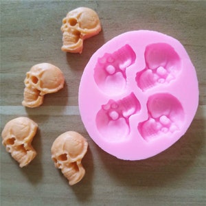 Pode incluir: Forma de silicone rosa com quatro cavidades em forma de caveira. Também são mostradas cinco pequenas balas em forma de caveira de cor laranja.