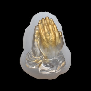 May include: A white silicone mold of two hands clasped in prayer. The hands are painted gold.