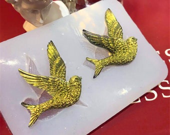 Può includere: Due stampi per uccelli dorati in uno stampo di silicone bianco. Gli uccelli sono in posizione di volo con le ali spiegate.
