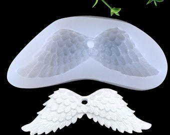 May include: A white silicone mold for making angel wings. The mold is shaped like a pair of wings with detailed feathers. A pair of white angel wings made with the mold is shown below.
