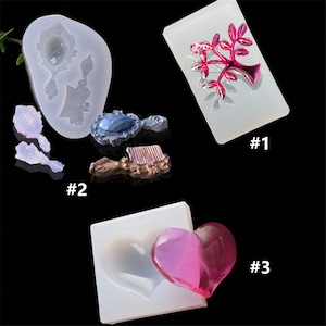 May include: Three silicone moulds for resin crafts. The first mould is rectangular and features a pink tree design. The second mould is oval and features a mirror and comb design. The third mould is square and features a heart shape.