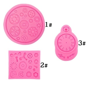 Può includere: Tre stampi in silicone rosa per la cottura. Il primo stampo è un cerchio con un disegno di ingranaggi. Il secondo stampo è un quadrato con un disegno di ingranaggi e altre piccole forme. Il terzo stampo è un orologio da tasca con numeri romani.