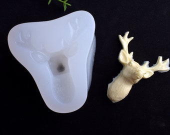 May include: A white silicone mold shaped like a deer head, next to a finished deer head made from a light brown material.