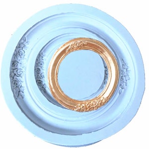 May include: A white silicone mould for making a round cake or dessert with a decorative frame. The mould has a raised design of roses around the outer edge and a smaller, raised frame in the centre.