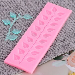 May include: Pink silicone mould with a design of a row of leaves. The mould is on a grey textured surface.