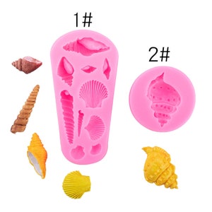 Könnte beinhalten: Zwei rosa Silikonformen zum Herstellen von Muschel-förmigen Leckereien. Die erste Form hat 10 verschiedene Muschelformen. Die zweite Form hat eine große Muschelform. Die Formen sind mit "1#" und "2#" gekennzeichnet.