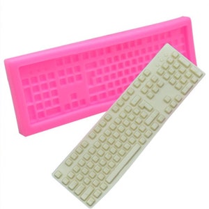 May include: Pink silicone mould for making a keyboard-shaped cake or other edible creations. The mould is shown with a white keyboard-shaped cake inside.