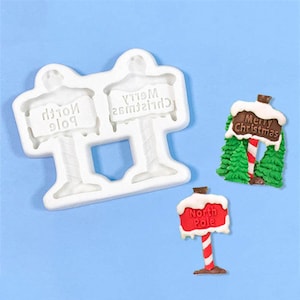 Peut inclure: Moule en silicone blanc pour la fabrication de décorations de gâteaux sur le thème de Noël. Le moule comprend deux panneaux qui indiquent "Joyeux Noël" et "Pôle Nord" et un panneau avec un bonhomme de neige et le texte "Joyeux Noël".