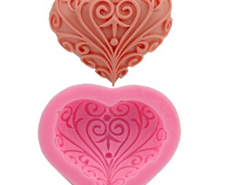 May include: Pink silicone mould shaped like a heart with a detailed, intricate design. The mould is designed to create a heart-shaped cake or chocolate decoration.