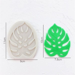 Op de afbeelding: Een siliconen mal en een groen plastic blad in de vorm van een monstera plant. De mal is 9 centimeter breed, 11 centimeter hoog en het blad is 7,8 centimeter breed en 10 centimeter hoog.