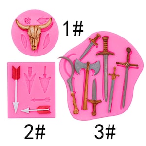 May include: Pink silicone moulds featuring a bull skull, arrows, and various medieval weapons. The moulds include a bull skull with horns, arrows with different arrowhead designs, and swords, axes, and knives. The numbers "1#", "2#", and "3#" are printed on the image.