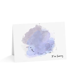 May include: A folded white greeting card with a watercolour design in shades of purple and blue. The card features the text "I'm Sorry" in black script.