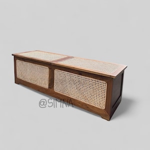 Puede incluir: Un banco de almacenamiento de madera rectangular y largo con una parte superior y paneles frontales de caña tejida. El banco está teñido de color marrón oscuro y tiene un diseño moderno. Incluye el texto "@SIMNA".