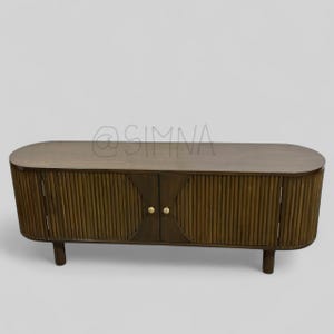 May include: A dark brown wooden media console with two doors and a curved top. The doors have vertical grooves and gold-toned knobs.
