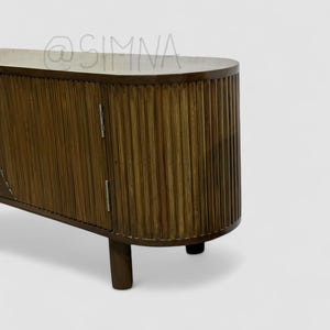 May include: A dark brown wooden cabinet with two doors and a curved top. The doors have vertical grooves and are closed. The cabinet is on four short legs.