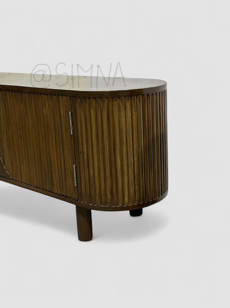 May include: A dark brown wooden cabinet with two doors and a curved top. The doors have vertical grooves and are closed. The cabinet is on four short legs.