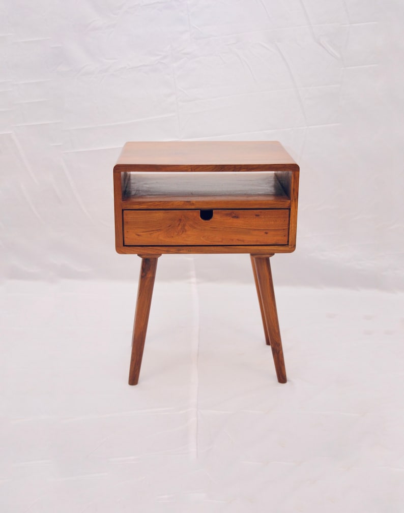 May include: A wooden end table with a single drawer and a shelf. The table has a light brown finish and four tapered legs.