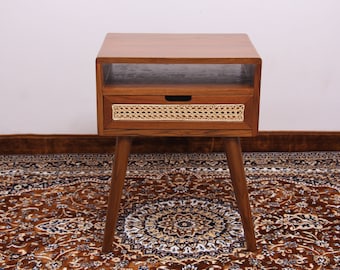 Puede incluir: Una mesa auxiliar de madera con un cajón y un estante. El frente del cajón está hecho de ratán tejido y las patas son cónicas.