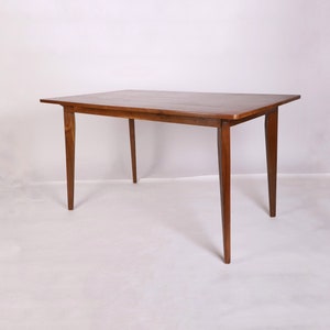 Könnte beinhalten: Ein rechteckiger Holztisch mit vier Beinen. Der Tisch ist aus dunkelbraunem Holz und hat eine glatte, polierte Oberfläche.