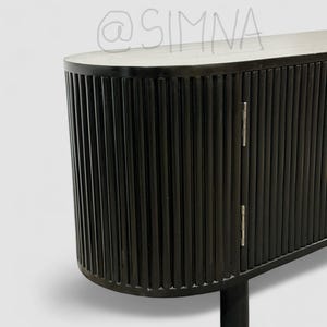 May include: Black wooden cabinet with vertical grooves and rounded edges. The cabinet has two doors with silver hinges and sits on short legs.