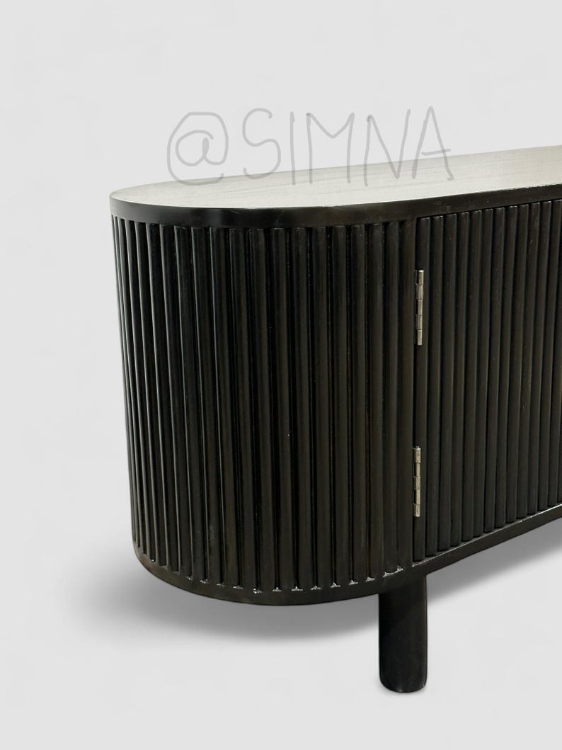 May include: Black wooden cabinet with vertical grooves and rounded edges. The cabinet has two doors with silver hinges and sits on short legs.