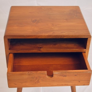 May include: A wooden bedside table with a drawer and a shelf. The drawer is open and the shelf is empty.