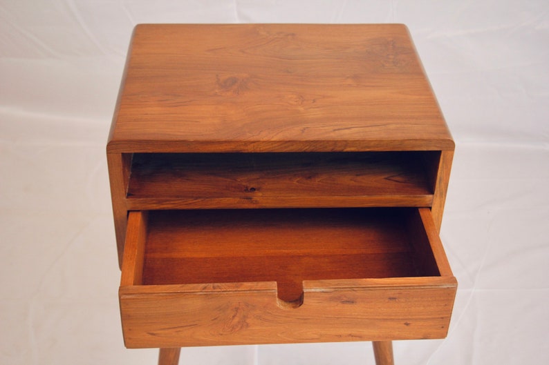 May include: A wooden bedside table with a drawer and a shelf. The drawer is open and the shelf is empty.