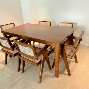 Puede incluir: Una mesa de comedor de madera con seis sillas. La mesa es de madera oscura y tiene forma rectangular. Las sillas también son de madera y tienen asientos de mimbre tejido.