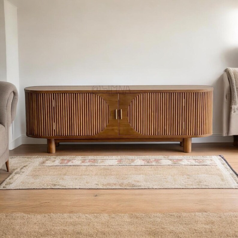May include: A mid-century modern style wooden media console with two doors and vertical slat detailing. The console has a rounded front and sits on a rug.