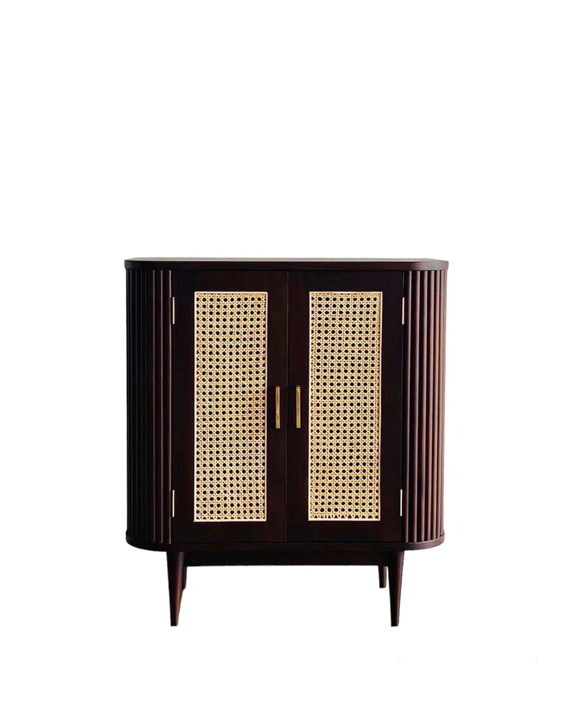 May include: A dark brown wooden cabinet with two doors featuring woven cane panels. The cabinet has a curved top and bottom and sits on four slender legs.