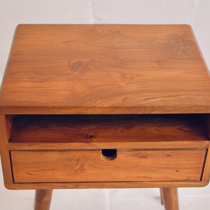 May include: A wooden bedside table with a drawer and a shelf. The table has a light brown finish and a simple design.