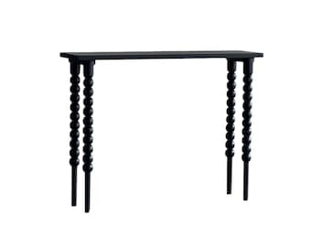 Puede incluir: Una mesa consola negra con una tapa rectangular y patas con cuentas.