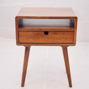 May include: A wooden end table with a single drawer and a shelf. The table has a light brown finish and four tapered legs.