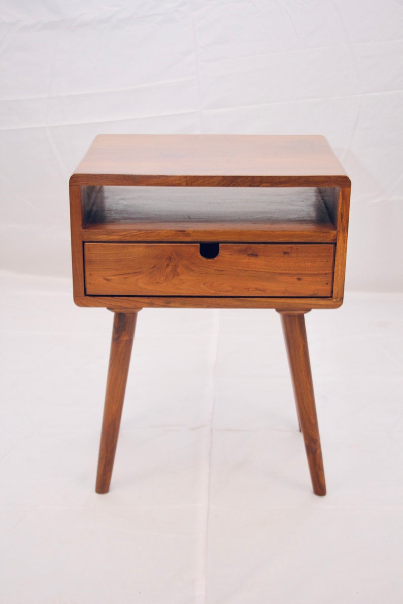 May include: A wooden end table with a single drawer and a shelf. The table has a light brown finish and four tapered legs.